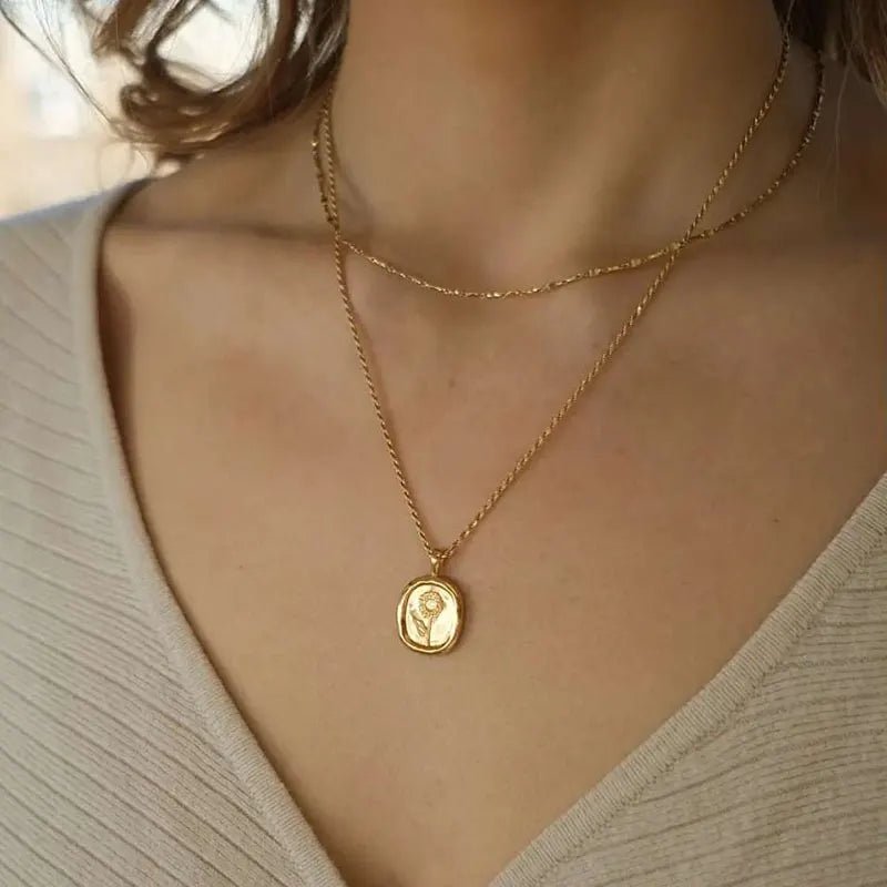 Gold necklace with a pendant on a person wearing a beige top.