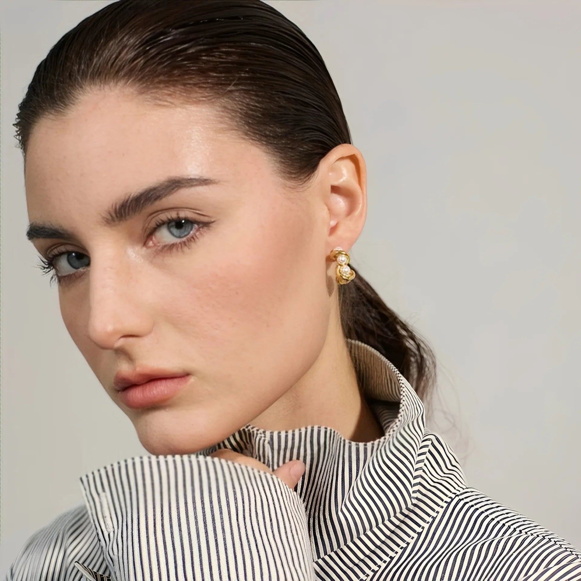 Close-up of a woman wearing gold earrings with a neutral background