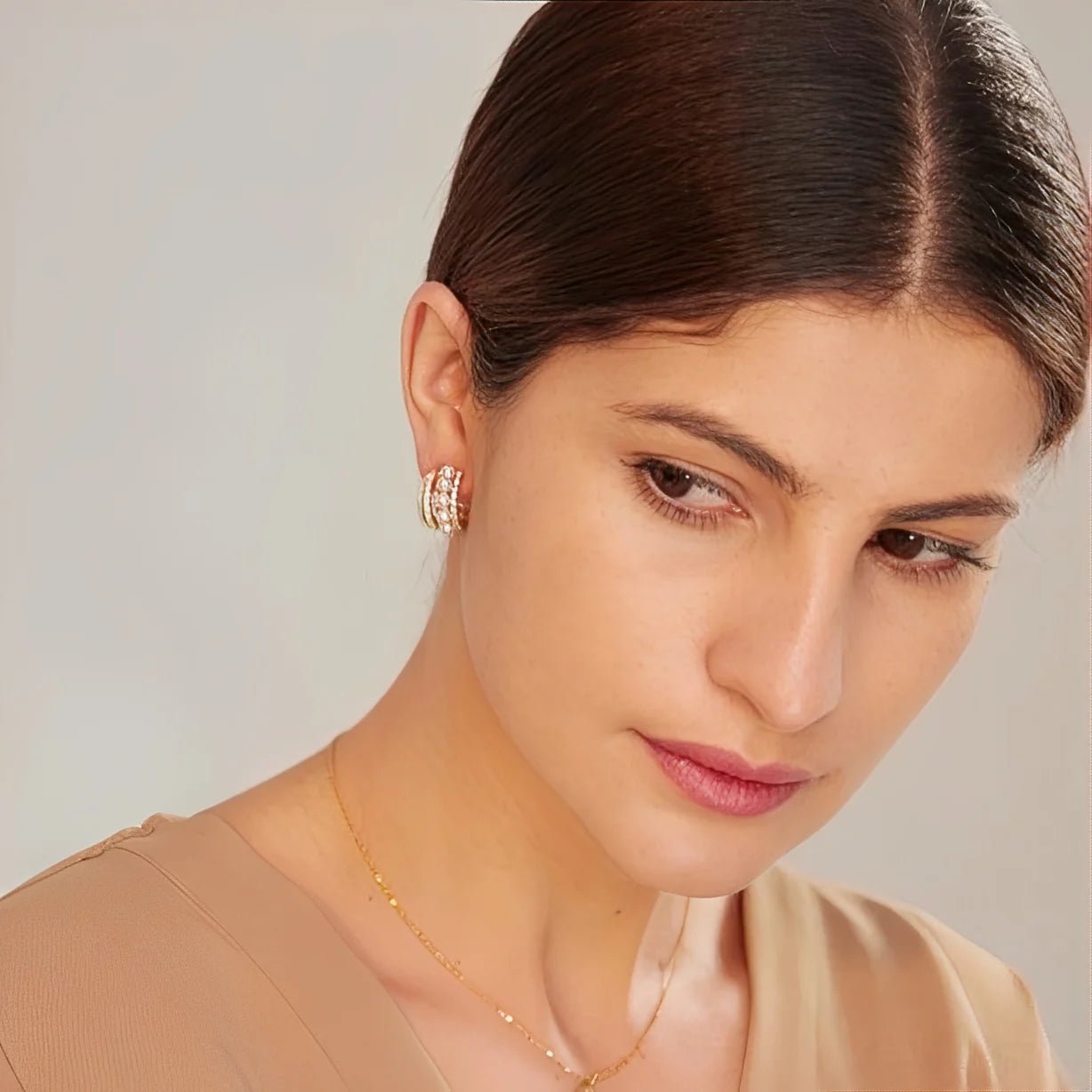 Close-up of a woman wearing earrings and a necklace against a neutral background