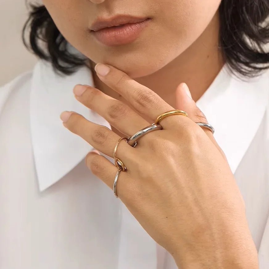 Close-up of a person wearing multiple gold rings on a white shirt background