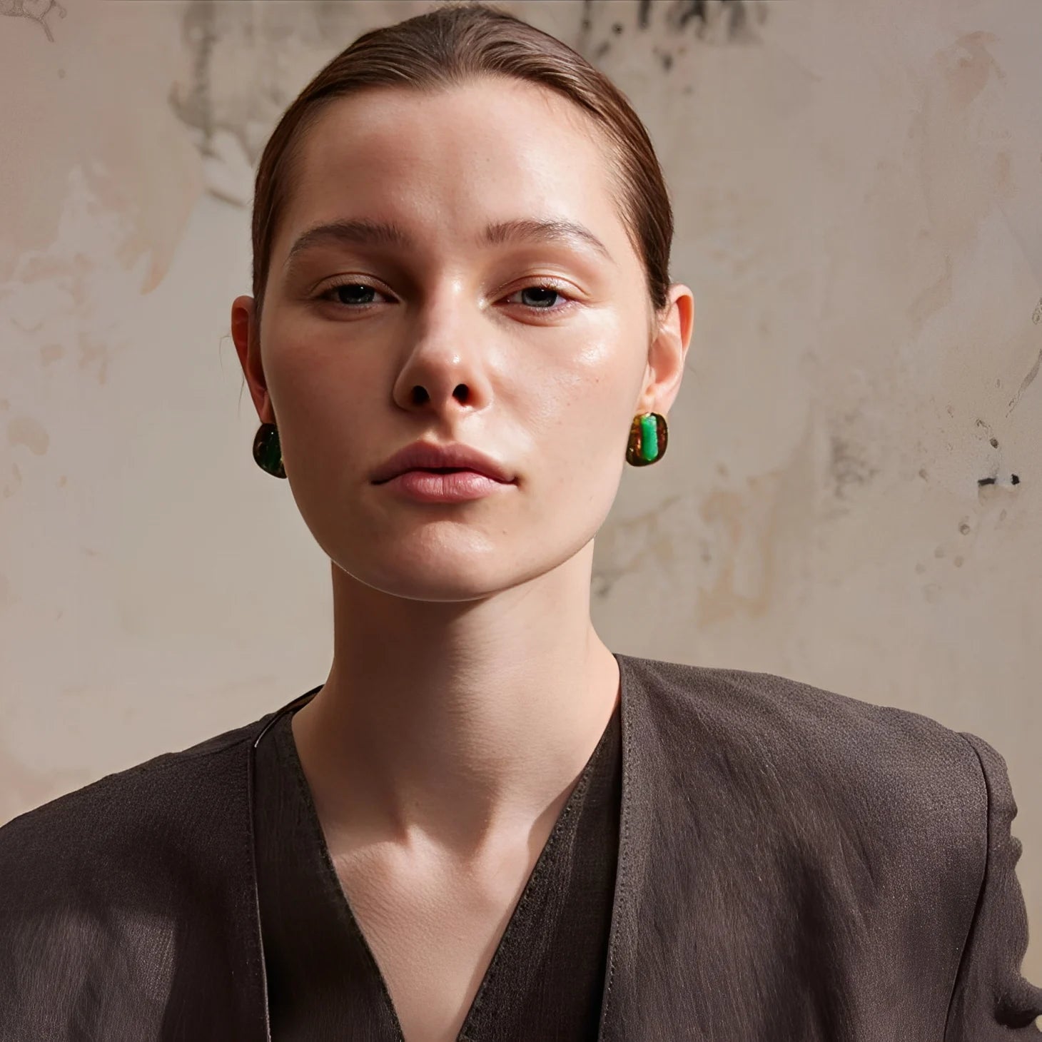 Woman wearing green earrings against a textured beige background