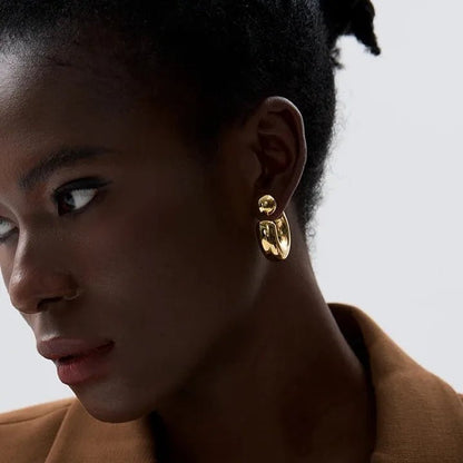 Close-up of a woman wearing gold hoop earrings with a neutral background