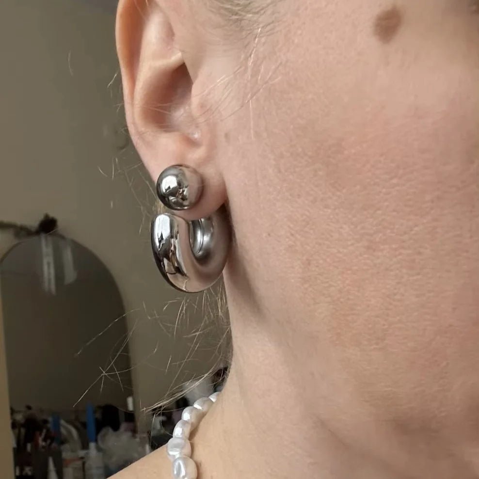 Close-up of an ear wearing silver hoop earrings with a blurred background.