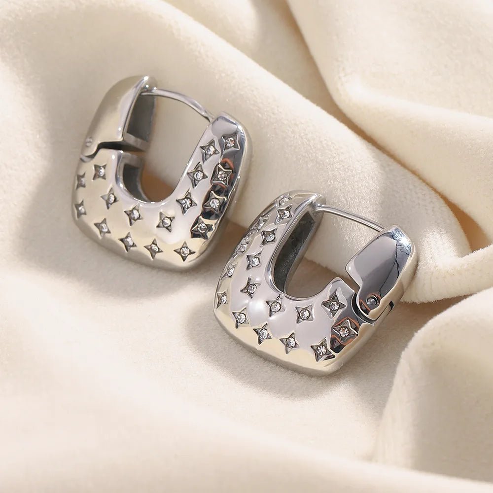 Silver hoop earrings with star-shaped stones on a beige fabric background